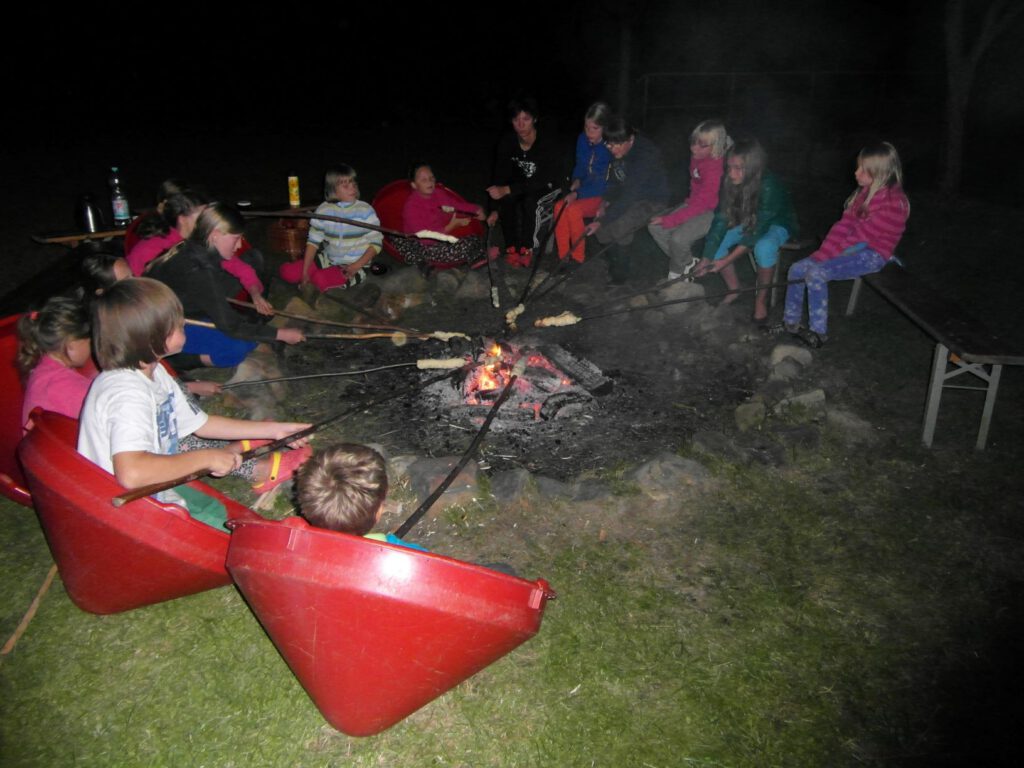 Kinder sitzen mit Stockbrot um ein Lagerfeuer